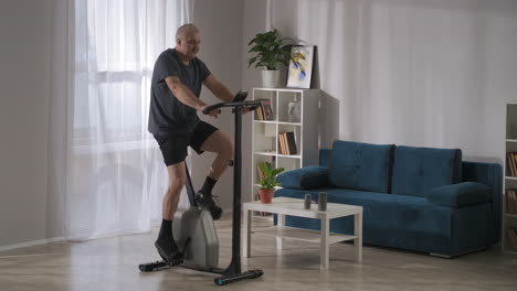 training-on-exercise-bike-for-losing-weight-and-keeping-physical-condition-middle-aged-man-is-spinning-pedals-at-home